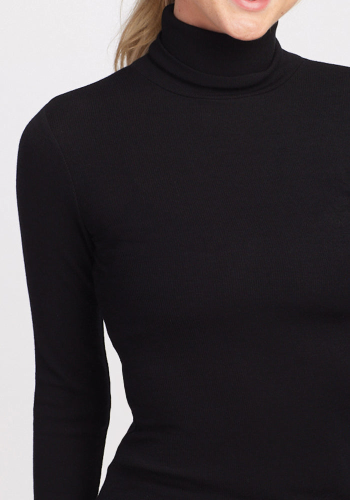 A person in a black Sage Ribbed Turtleneck from Woolx stands against a light gray background, with only the upper body and part of the neck visible, highlighting the flattering fit.
