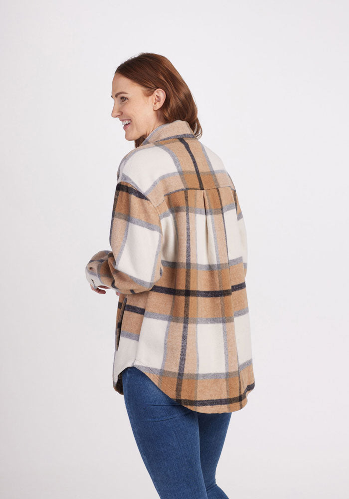 A woman with brown hair smiles and looks to the side, wearing the Woolx Sawyer Shacket - Camel Plaid and blue jeans, standing against a plain white background.