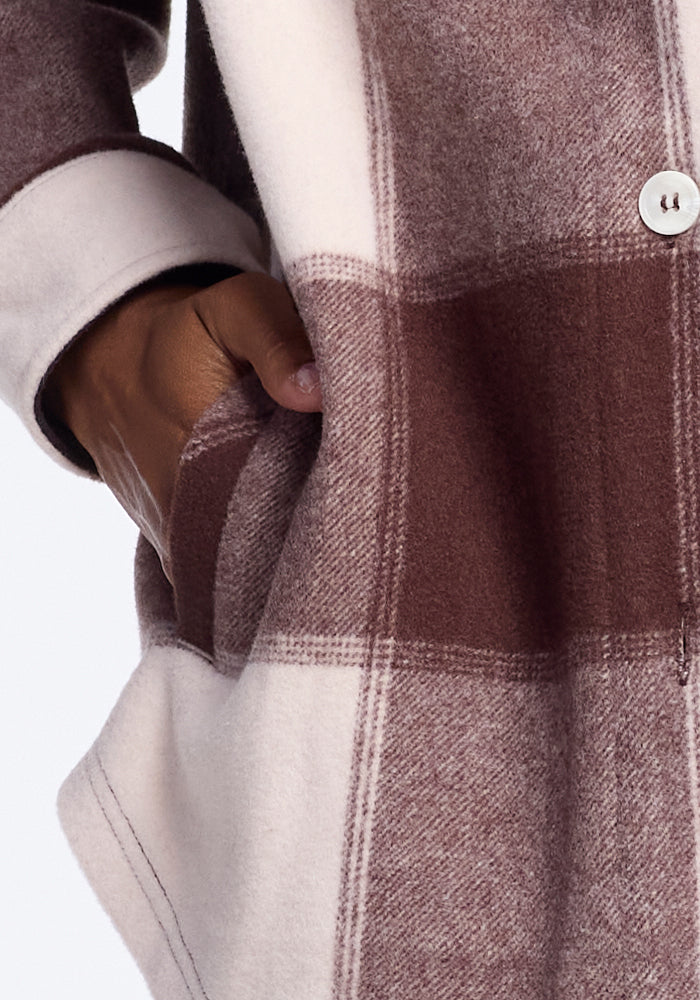 A close-up of a hand in the pocket of the Woolx Sawyer Shacket in Chai Latte Plaid, featuring large buttons.