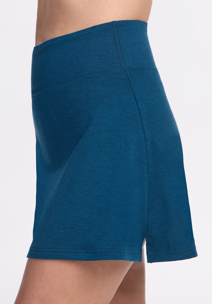 Side view of a person wearing the Woolx Sienna Skort in Majolica Blue, featuring a high waist and knee-length cut with a small side slit, set against a plain white background.