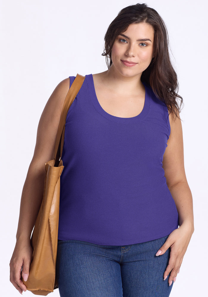 A woman in a Woolx Sloane Ribbed Tank - Berry Indigo and blue jeans holds a tan shoulder bag against a white background. | Juliana is 5'10", wearing a size XL