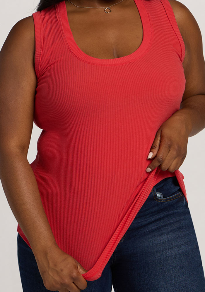 A person in the Woolx Sloane Ribbed Tank - Hibiscus and dark blue jeans, holding the tank's hem.