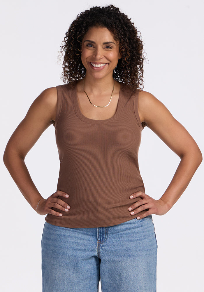 Smiling woman wears the Woolx Sloane Ribbed Tank in Sienna Kiss and blue jeans, posing hands on hips against white.