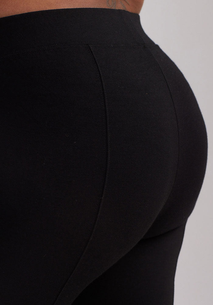 A person wearing the Stella Leggings - Black from Woolx is seen from behind, with attention on their lower back and hips. The sleek contouring fit of the leggings enhances their shape with flattering back seams, while the fabric appears smooth and fitted.