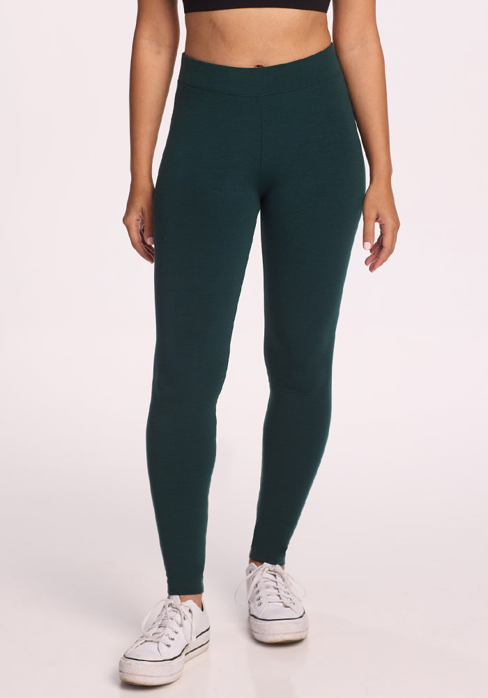 A person models Woolx's Stella Leggings in Deep Timber (Final Sale), paired with a black crop top and white sneakers, standing against a plain light background. The photo is cropped just below the shoulders.