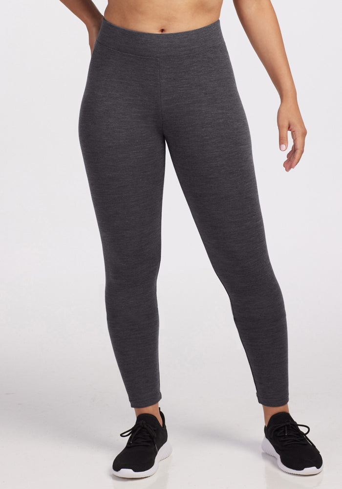 A person wearing Woolx Stella Petite - Cinder Melange high-waisted leggings stands against a plain white background. Only the lower torso and legs are visible. Black athletic shoes complete the look.