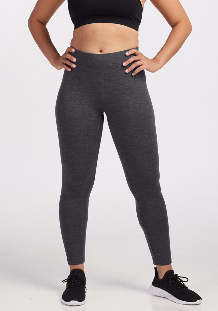 A person in a black sports bra, black athletic shoes, and Woolx Stella Petite - Cinder Melange leggings stands hands-on-hips against a plain white background.