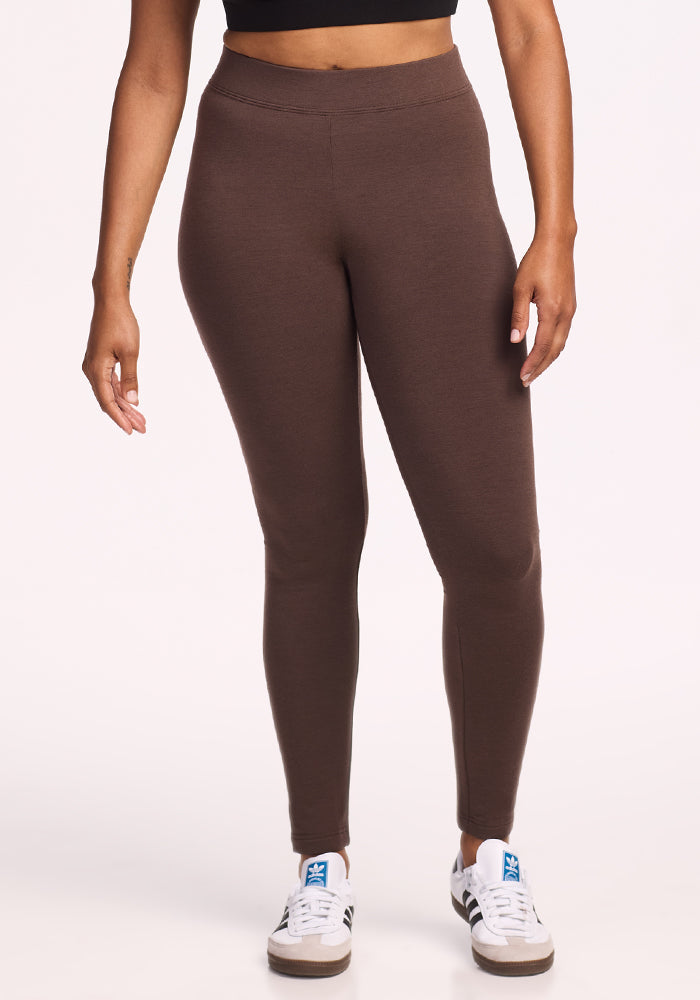 A person in the Woolx Stella Tall • Final Sale - Bracken leggings stands against a plain white background, paired with a black crop top and white sneakers with black stripes.