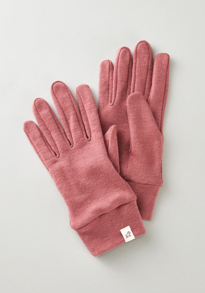 A pair of soft, pink Woolx Stone Harbor Gloves in Wild Ginger, featuring a small white tag on one cuff, displayed on a light gray surface. Final sale.