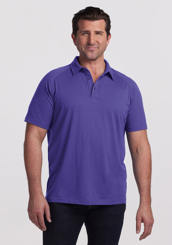 Man wearing the Woolx Summit Polo in Berry Indigo and dark jeans stands against a white background, facing the camera and smiling. | Brandon is 6’3.5”, wearing a size XL