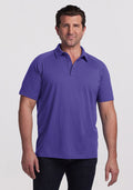 Man wearing the Woolx Summit Polo in Berry Indigo and dark jeans stands against a white background, facing the camera and smiling. | Brandon is 6’3.5”, wearing a size XL