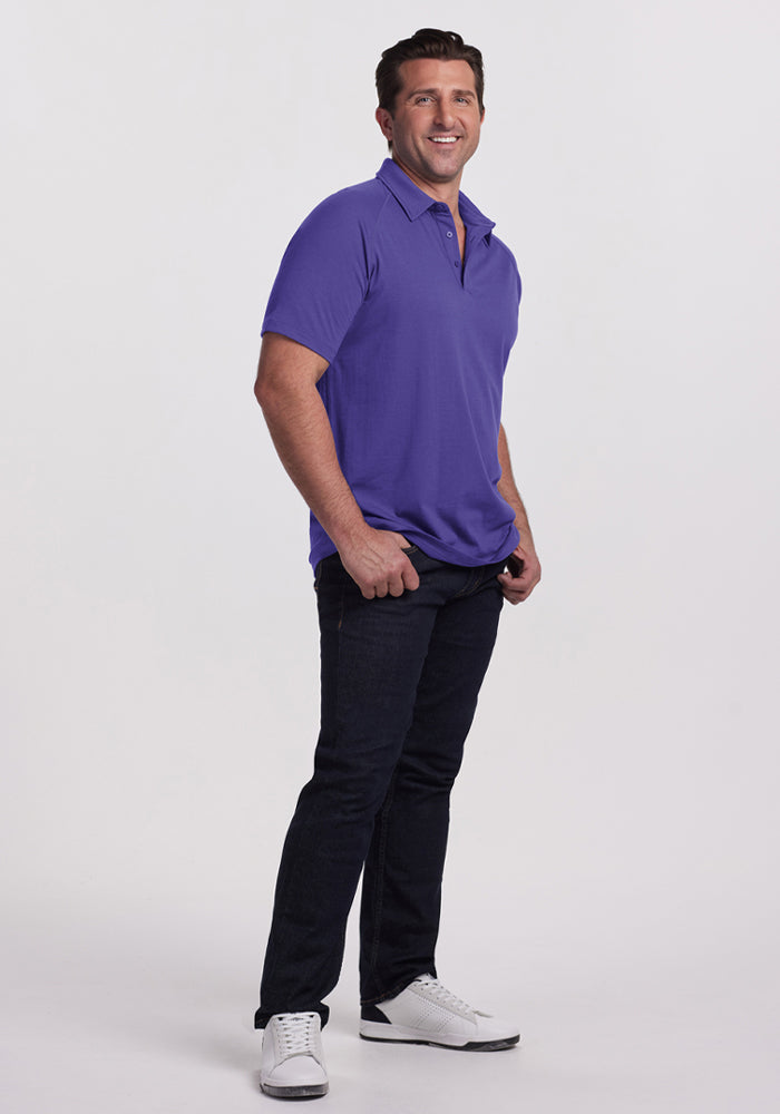 Man smiling in Woolx Summit Polo - Berry Indigo, dark jeans, and white sneakers against a plain white background.