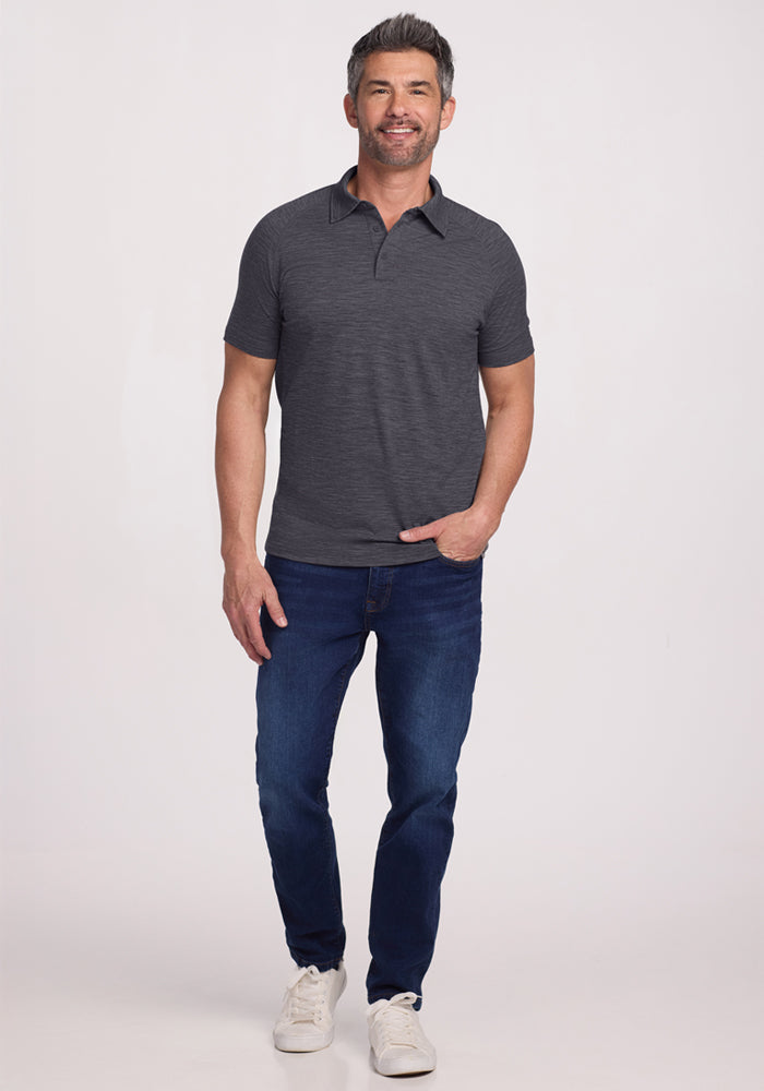 Smiling man in a Woolx Summit Polo • Final Sale - Cinder Melange and blue jeans stands against a light background.