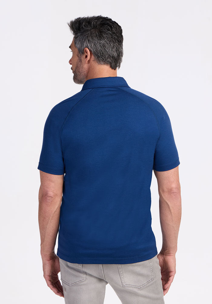 Man with short dark hair wears Woolx Summit Polo • Final Sale - Estate Blue and light gray jeans, shown from the back.
