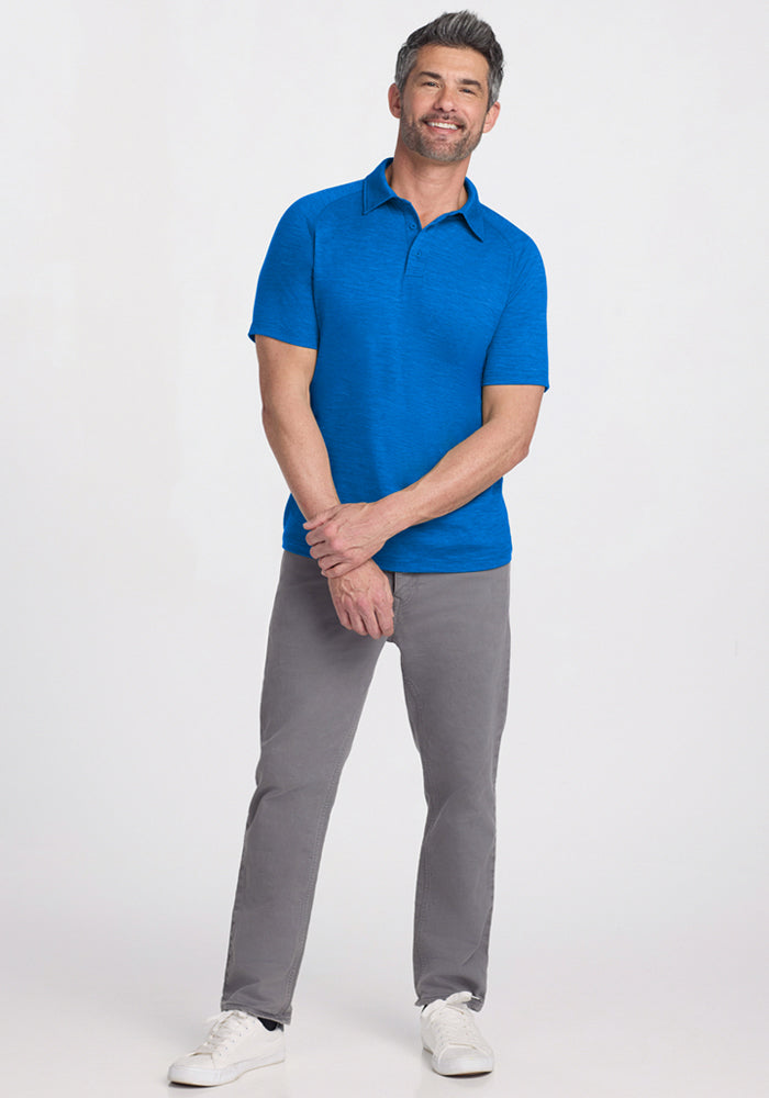 Smiling man in a Woolx Summit Polo • Final Sale - Glacial Blue, gray pants, and white sneakers against a light background.