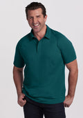 Smiling man in a Woolx Summit Polo • Final Sale - Riverbank Green and dark jeans stands against a light background.