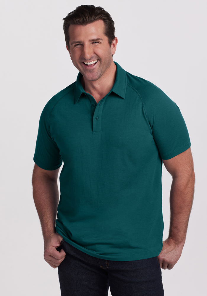 Smiling man in a Woolx Summit Polo • Final Sale - Riverbank Green and dark jeans stands against a light background.