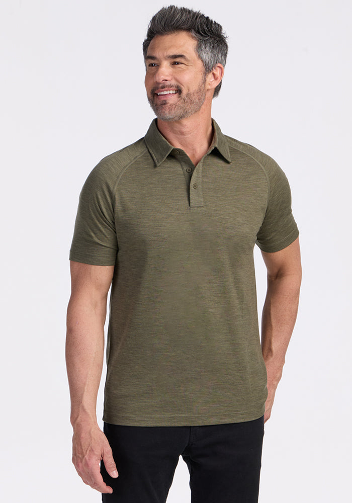 Smiling man in a Woolx Summit Polo, Sage Olive Melange, stands in black pants against a white background.