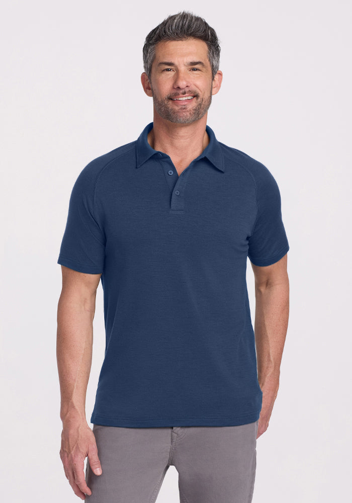 Man wears Woolx Summit Polo in Starry Night and gray pants, smiling confidently in high-performance athletic gear.