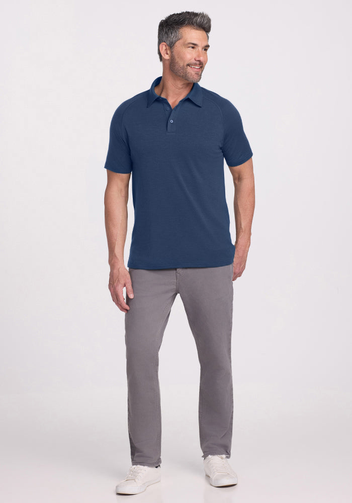 A man wears the Woolx Summit Polo in Starry Night, gray pants, and white sneakers, smiling against a light background.