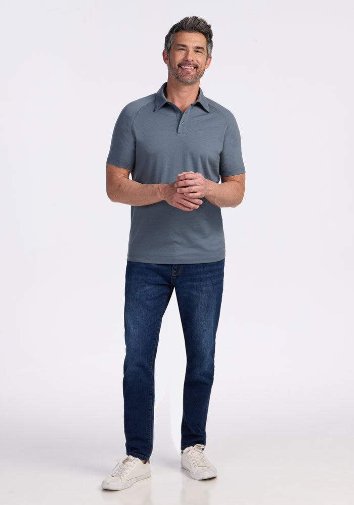 Smiling man in a Woolx Summit Polo • Final Sale - Stormy Weather, blue jeans, and white sneakers against a white background.