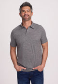 A man with short hair and a beard wears the Woolx Summit Polo in Graphite Heather with jeans, hands in pockets, smiling at the camera against a plain white background, highlighting the shirt's natural moisture management qualities. | Matthew is 6’, wearing a size L