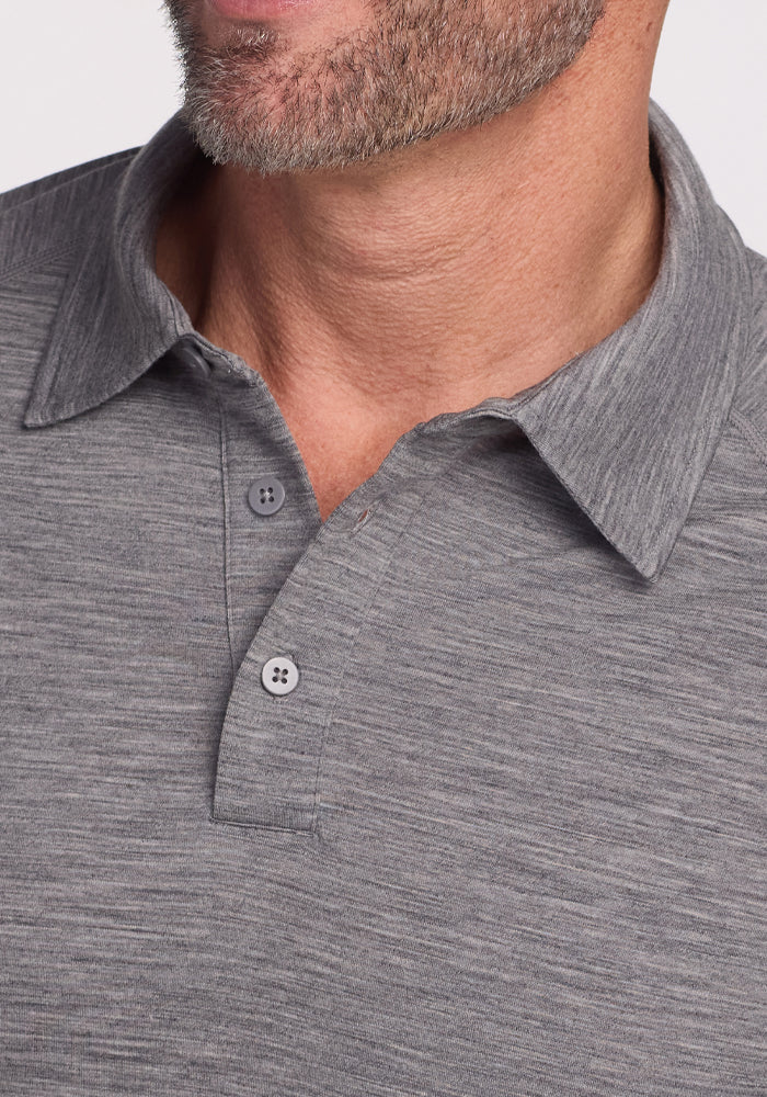 A close-up captures a person in the Summit Polo - Graphite Heather by Woolx, featuring Merino Wool for outstanding moisture control. The image reveals only the lower face, neck, and shoulders with a textured look and two buttons fastened, paired with the individual's neatly trimmed beard.
