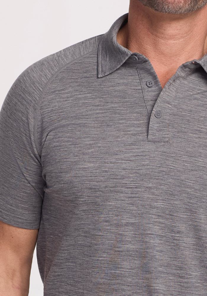 A person is wearing the Woolx Summit Polo in Graphite Heather. This grey short-sleeved Merino Wool shirt has a collar and two buttons near the neck, with visible stitching for moisture control. The image captures their upper body and part of their face, cropped above the nose.