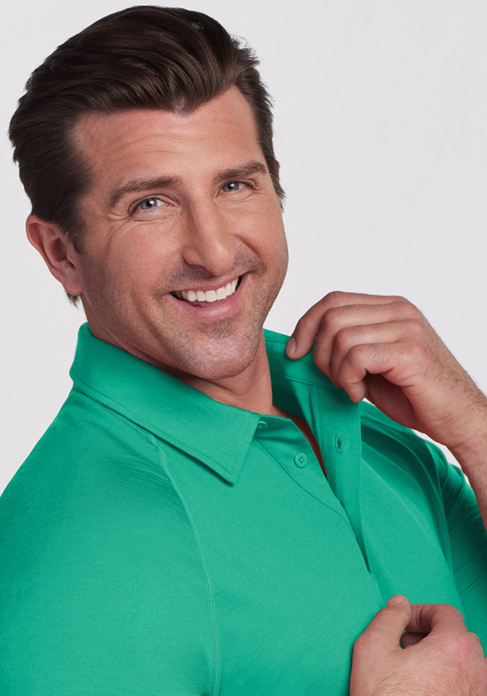 Smiling man in a Woolx Summit Polo - Jungle holds the collar, posing against a plain light background.