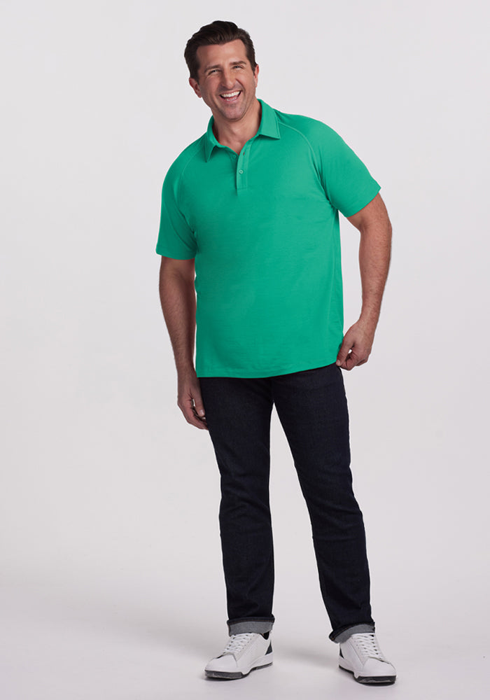 Man wearing Woolx Summit Polo - Jungle, dark jeans, and white sneakers, smiling against a plain white background.