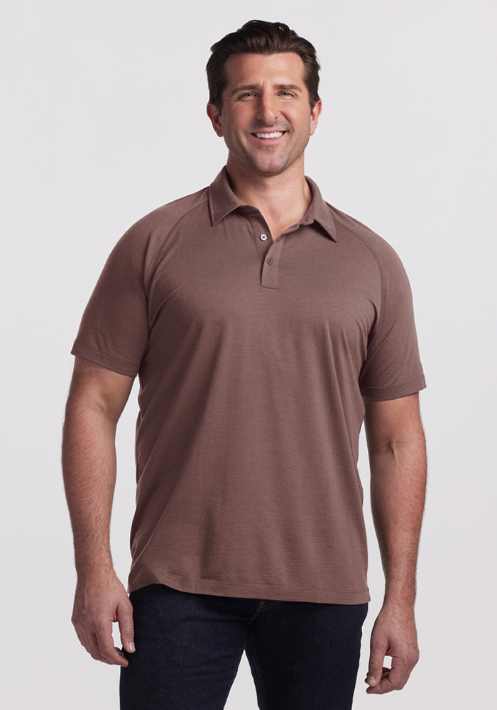 Smiling man wears a Woolx Summit Polo in Peppercorn and dark jeans against a plain light background. | Brandon is 6’3.5”, wearing a size XL