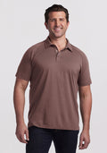 Smiling man wears a Woolx Summit Polo in Peppercorn and dark jeans against a plain light background. | Brandon is 6’3.5”, wearing a size XL