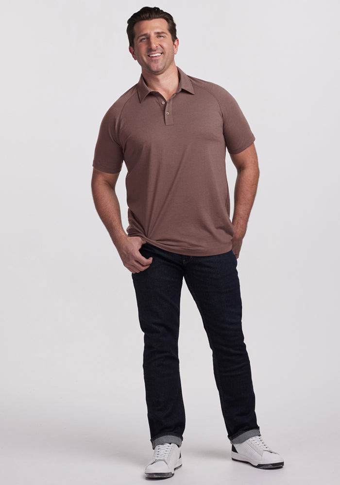 Man smiling, wearing Woolx Summit Polo - Peppercorn, dark jeans, and white sneakers against a plain background.