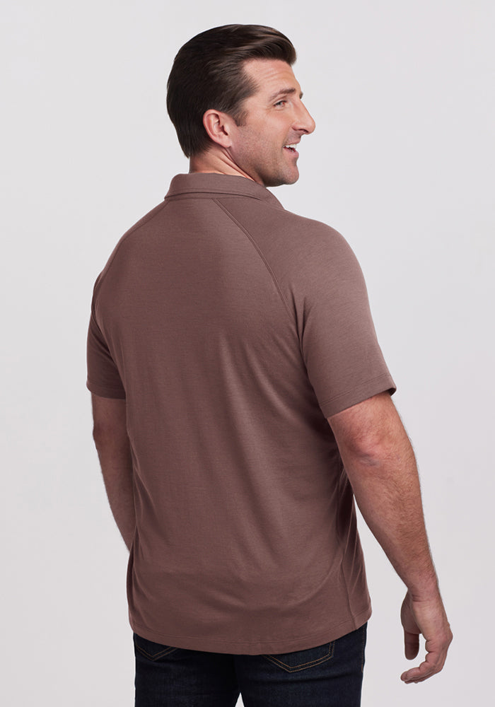 Man with short brown hair in a Woolx Summit Polo - Peppercorn and dark jeans, standing and smiling, facing away.
