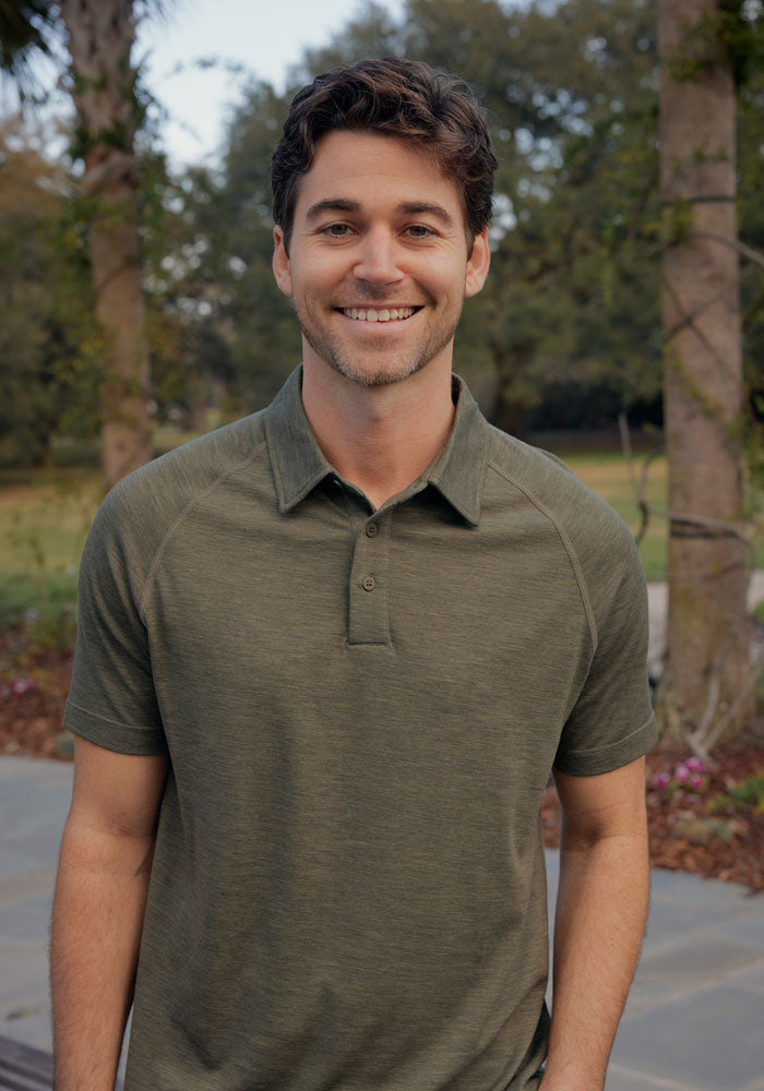 Man in a Woolx Summit Polo • Final Sale - Sage Olive Melange, standing outdoors with trees in the background.