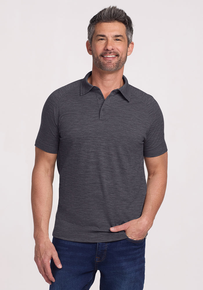 Smiling man with short dark hair wears the Woolx Summit Polo in Cinder Melange and blue jeans, against a plain background.