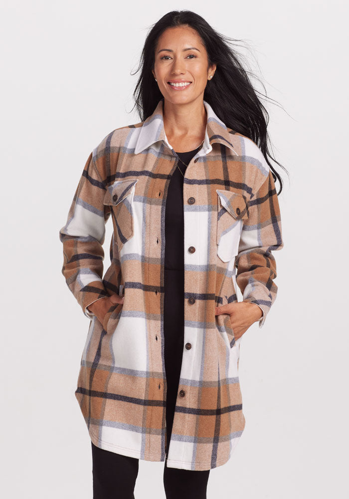 A woman smiling, wearing the Woolx Sutton Shacket in a Camel Plaid pattern. Made from premium merino wool in a regular fit, her hands rest in the pockets, complementing her long black hair against the plain white background.