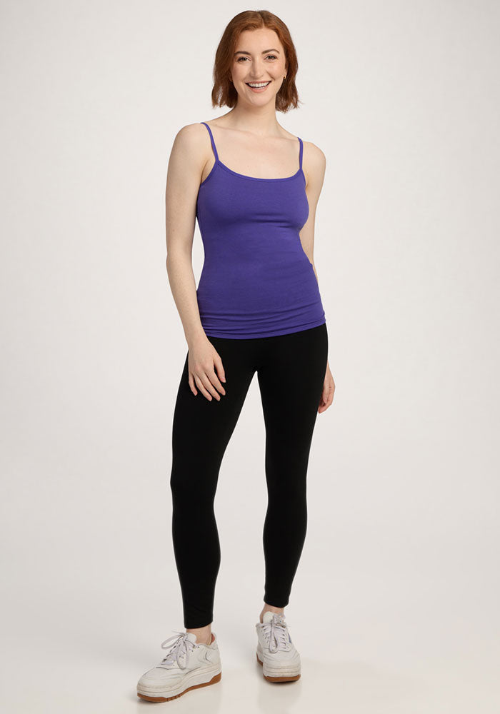 Smiling person wears the Woolx Teagen Cami With Shelf Bra in Berry Indigo, black leggings, and white sneakers.