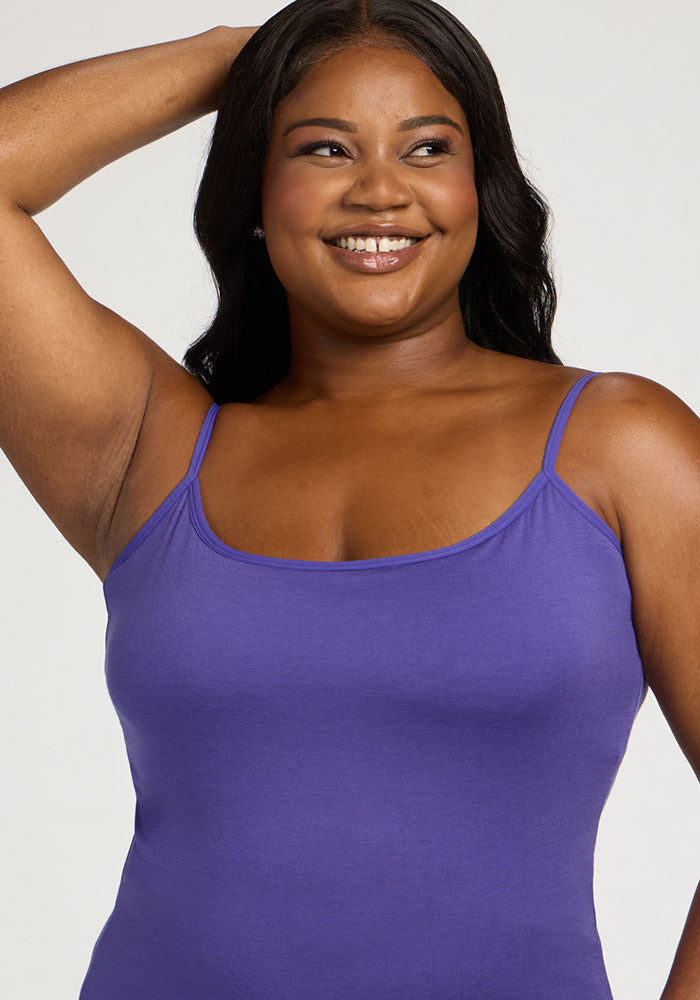 Smiling woman wearing Woolx Teagen Cami With Shelf Bra in Berry Indigo, one arm raised, against a plain background.
