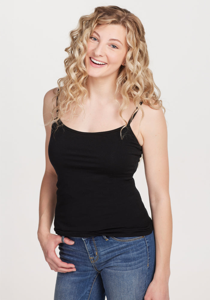 A smiling woman with long, curly blonde hair poses casually in a black Woolx Teagen cami featuring a built-in shelf bra and blue jeans against a plain white background, ideal for lightweight layering. | Jordan is 5'6", wearing a size S