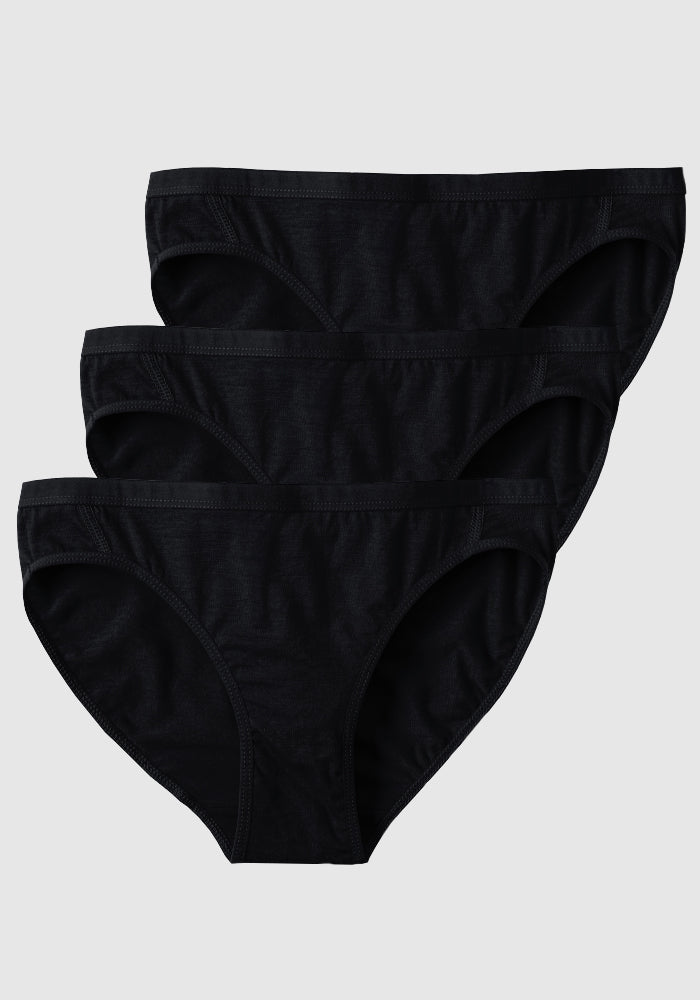 Three black Roxie Bikini panties by Woolx are stacked, slightly overlapping, against a plain gray background, each featuring a simple, classic cut.