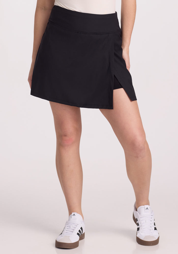 A person wearing the Topanga Skort - Black from Woolx and white sneakers stands against a plain white background. | Ariana is 5’11”, wearing a size S