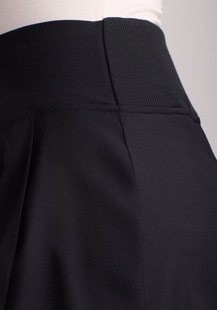 A person wears the Topanga Skort - Black by Woolx, highlighting a textured panel on the waistband. The garment fits snugly, with smooth fabric against a neutral backdrop.