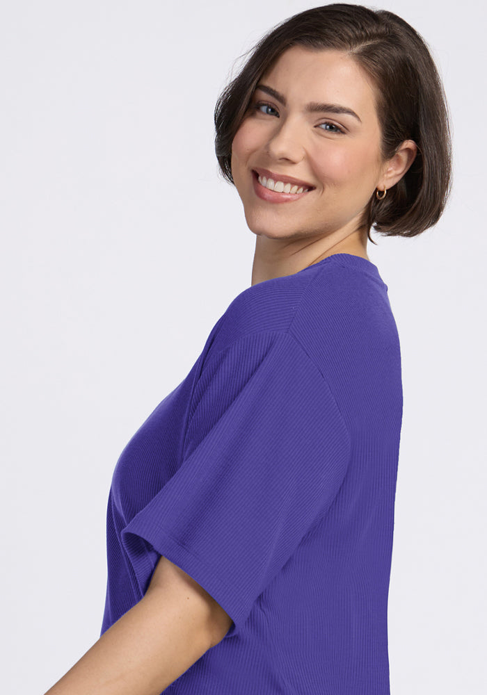 Woman with short brown hair smiles in the Woolx Vera Ribbed Tunic in Berry Indigo, posing against a plain background.
