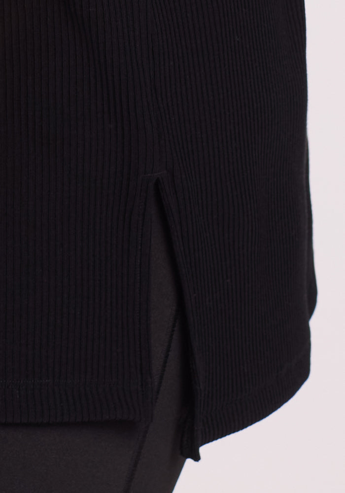 Close-up of the Woolx Vera Ribbed Tunic in black, featuring merino wool fabric, ribbed texture, side slit detail, and relaxed fit, styled over black pants.