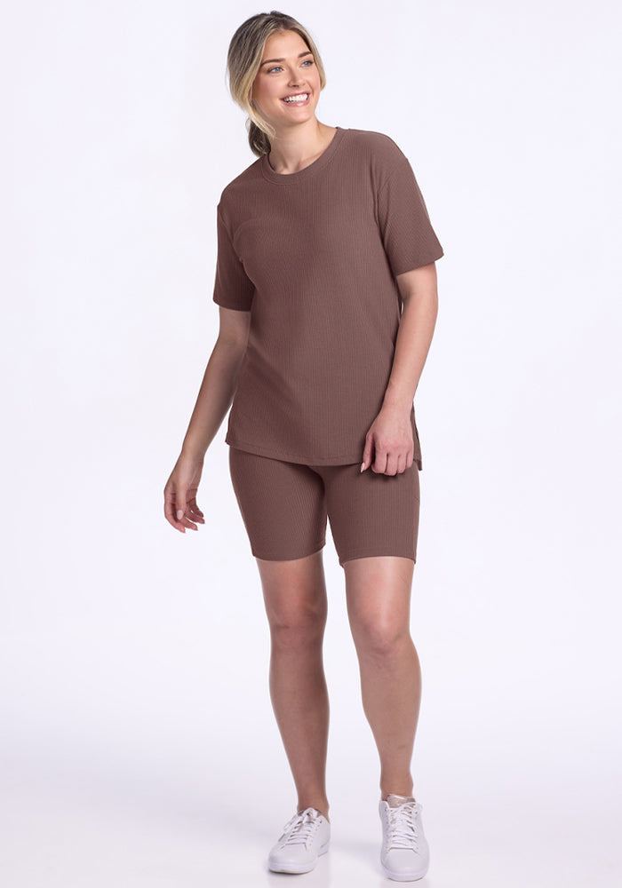 Woman wears the Woolx Vera Ribbed Tunic in Peppercorn, smiling in white sneakers against a white background.