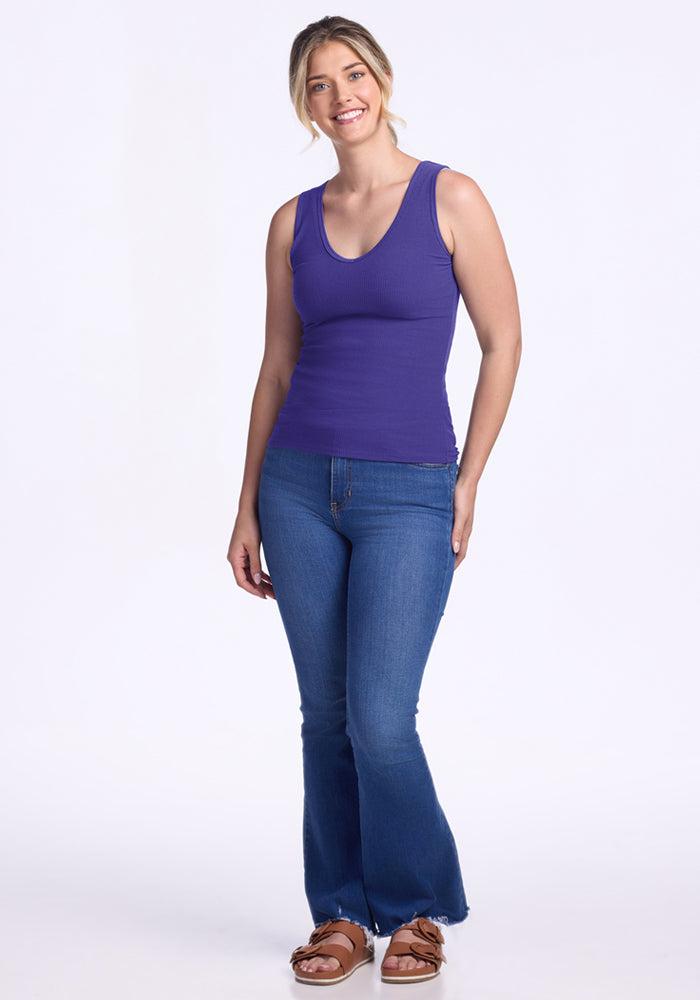 Smiling woman wears the Woolx Vivi Ribbed Tank - Berry Indigo with blue jeans and sandals against a white background.