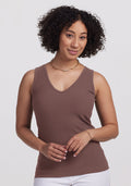Woman with curly hair wears the Woolx Vivi Ribbed Tank in Peppercorn and white pants against a plain light background. | Tori is 5'7", wearing a size S