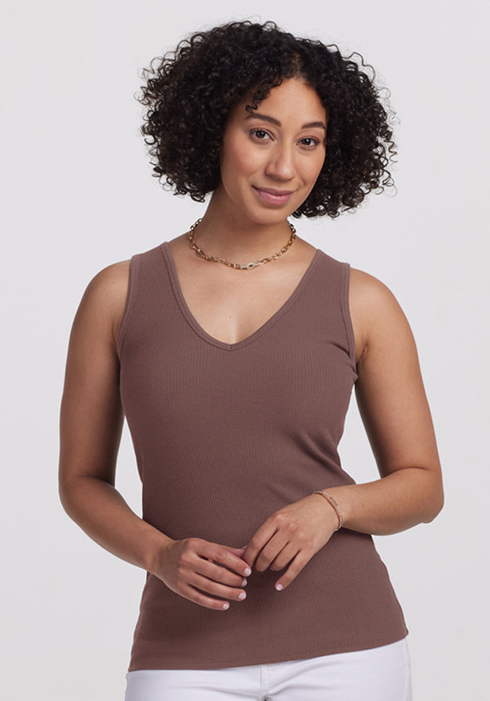 Woman with curly hair wears the Woolx Vivi Ribbed Tank in Peppercorn and white pants against a plain light background. | Tori is 5'7", wearing a size S