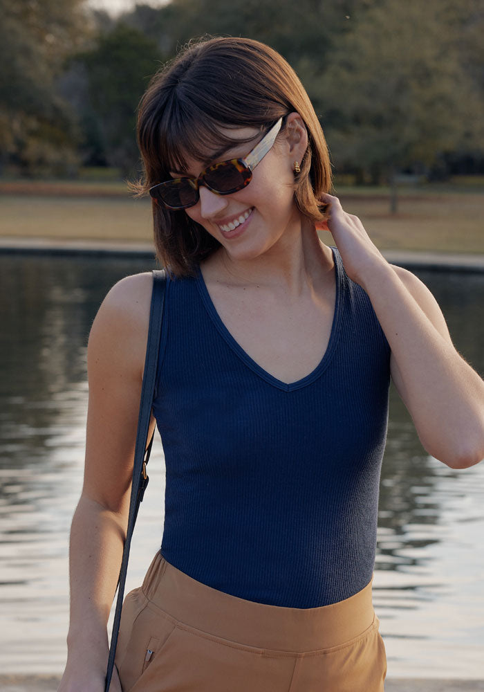 Woman in sunglasses wears the Woolx Vivi Ribbed Tank in Deep Navy, smiling by a lake in a park.